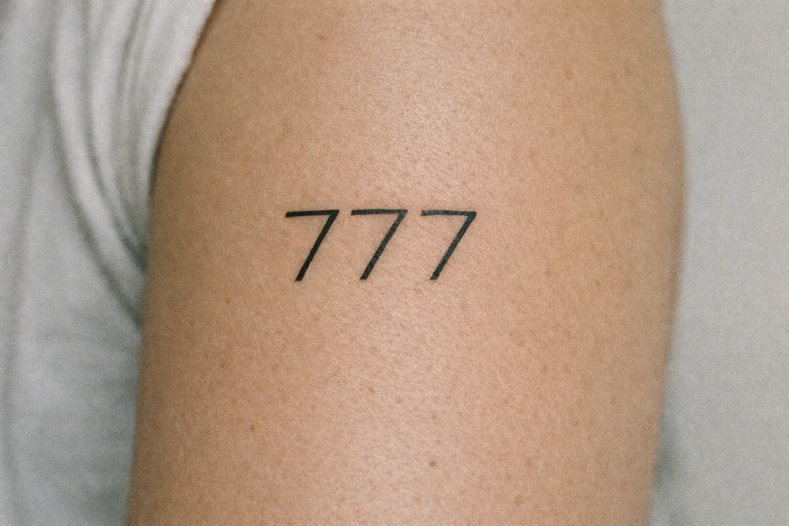 A person's upper arm with a '777' tattoo in bold black lines.