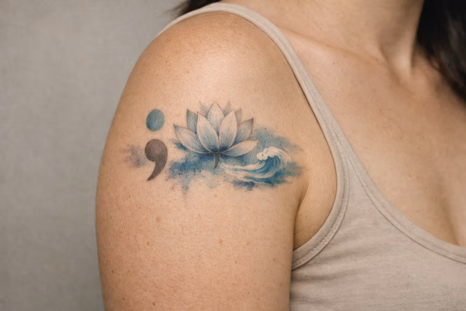 A person with a lotus flower, wave, and semicolon tattoo on their upper arm.