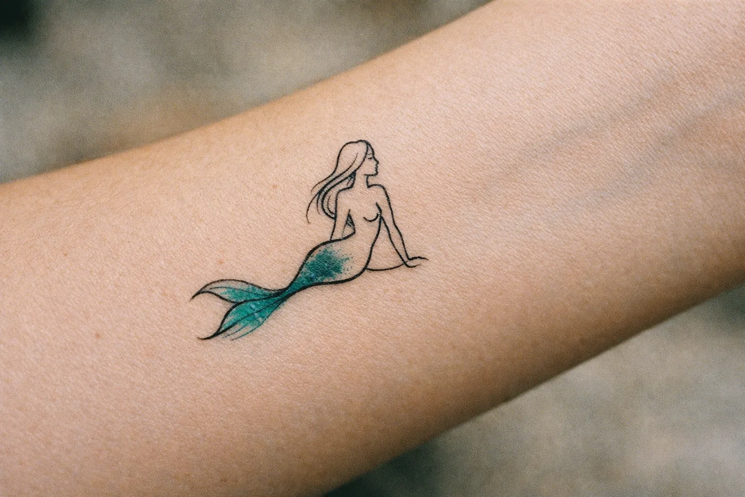Tiny minimalist mermaid silhouette tattoo on inner forearm