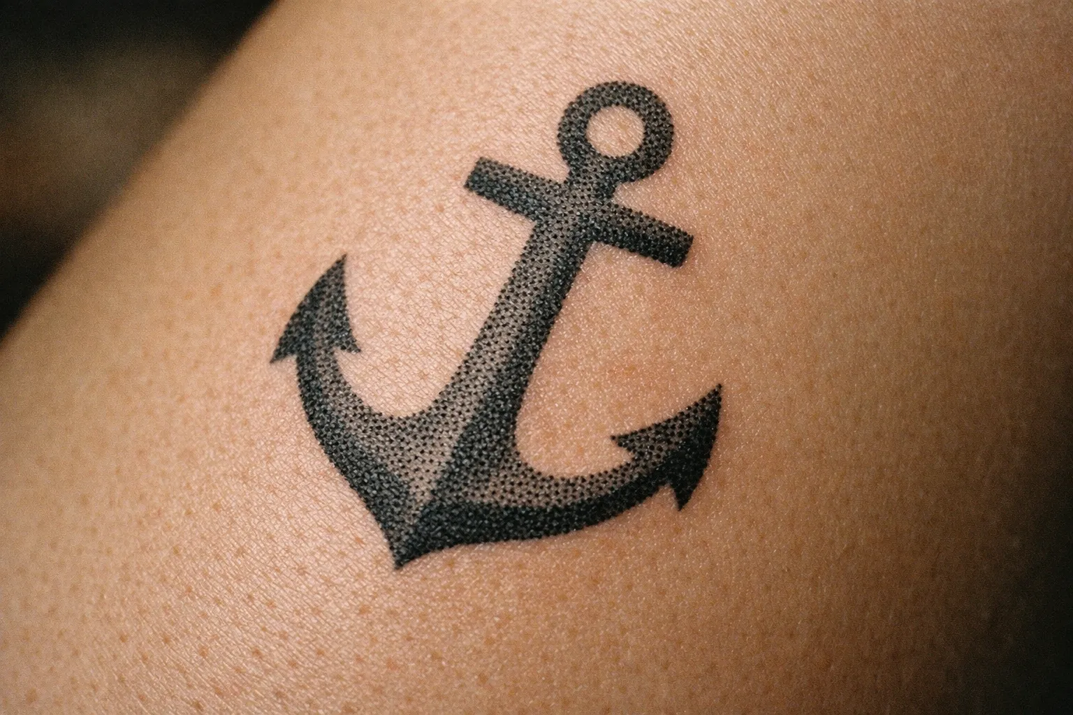 A black anchor tattoo on a person's skin.
