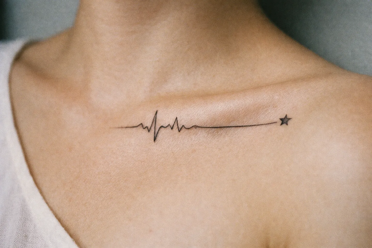 A person with a heartbeat and star tattoo near the collarbone.