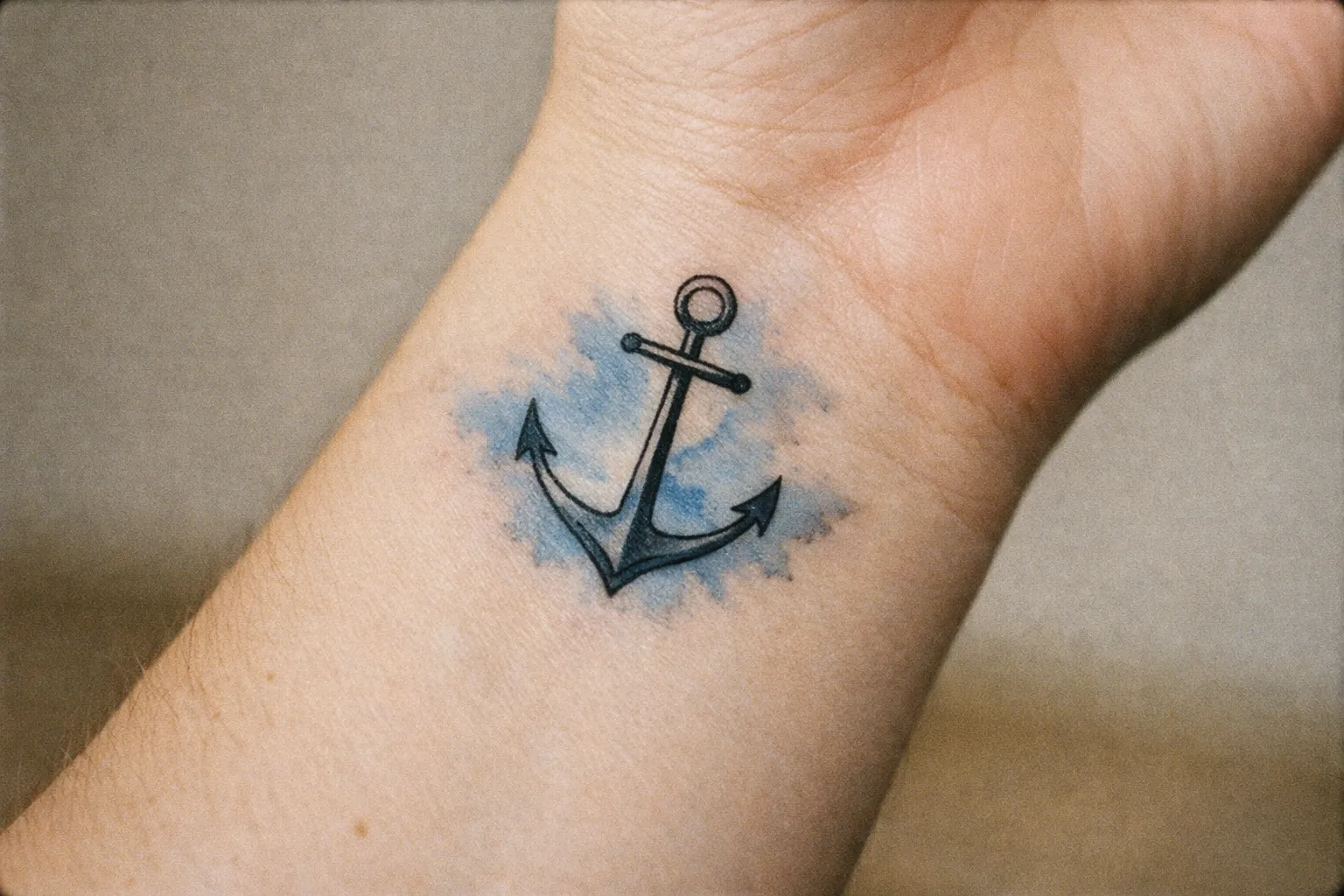 A person's wrist with an anchor tattoo over a blue watercolor background.