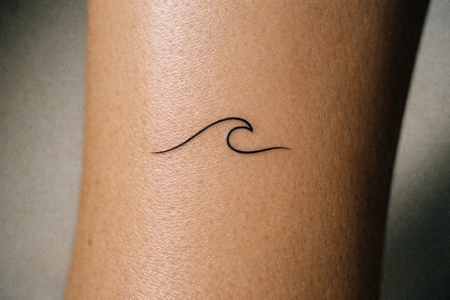 A simple wave tattoo is inked on a person's forearm.
