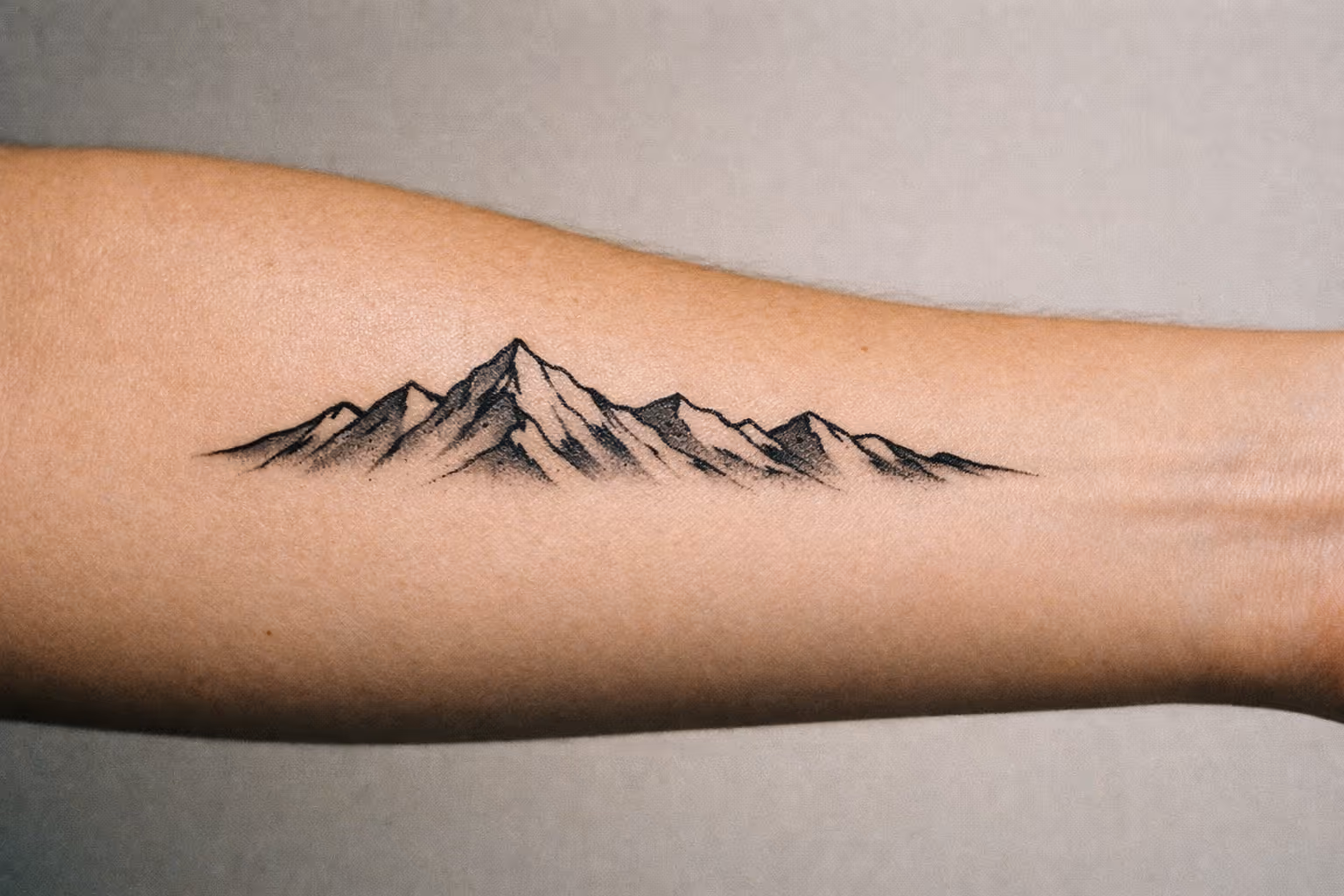 Editorial close-up of a mountain range tattoo on a forearm, showing crisp black linework and subtle shading