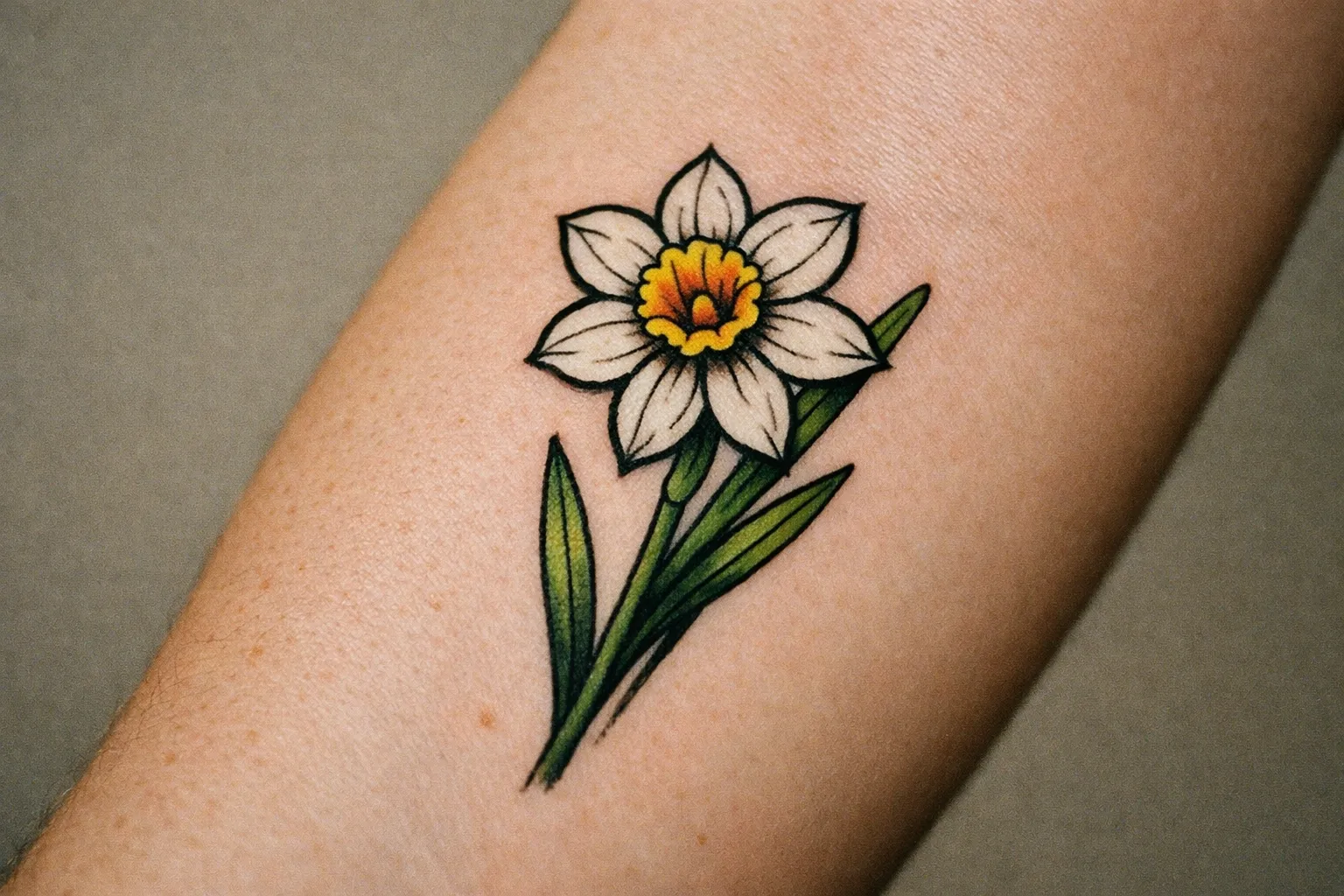 Macro shot of Narcissus flower tattoo on left forearm showing clean linework