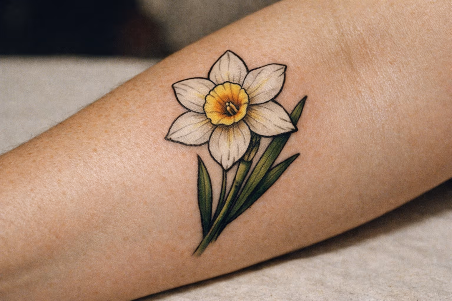 Editorial close-up of a Narcissus flower tattoo on forearm in studio light