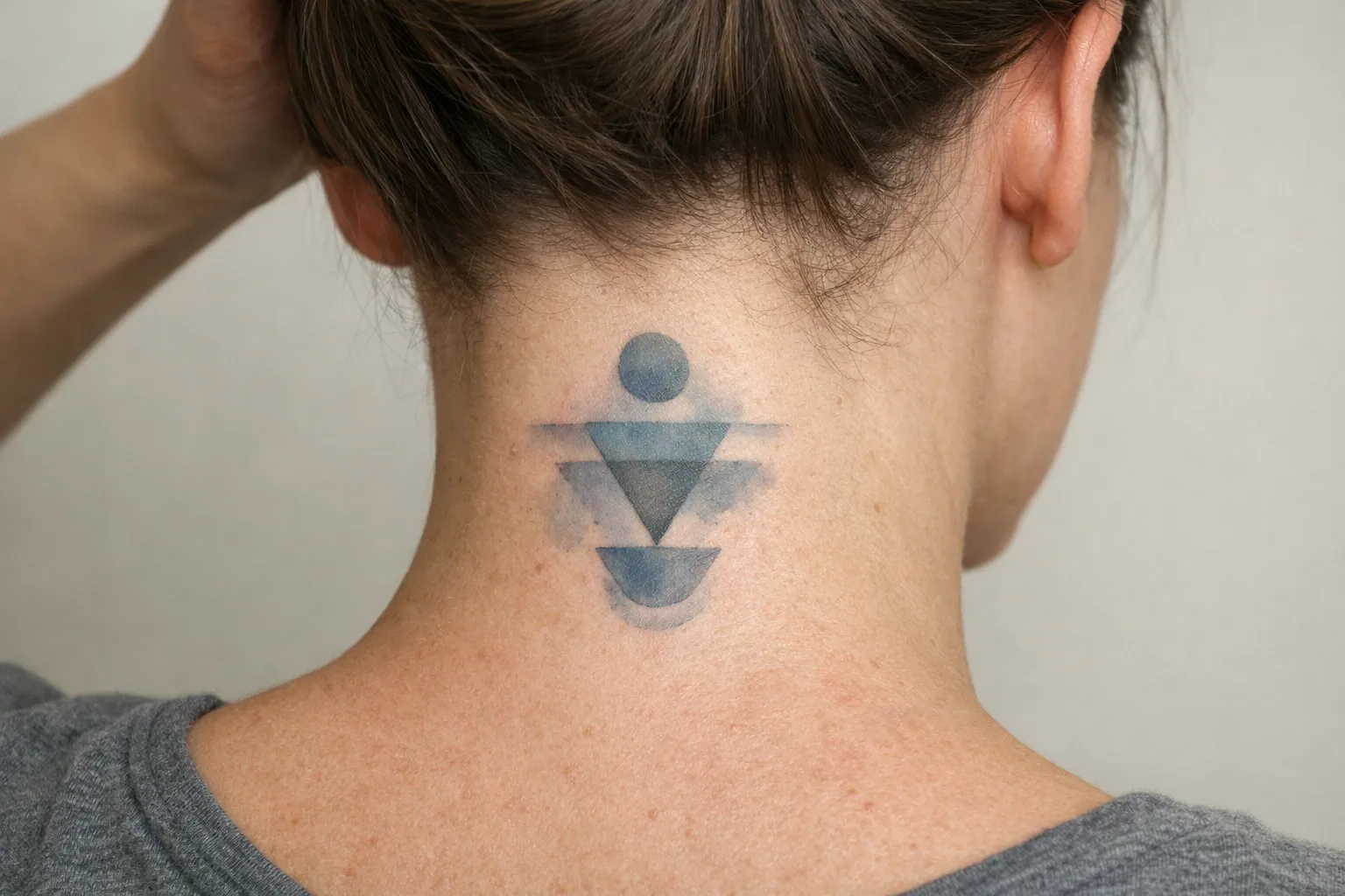 A person with geometric tattoo shapes on the back of their neck.