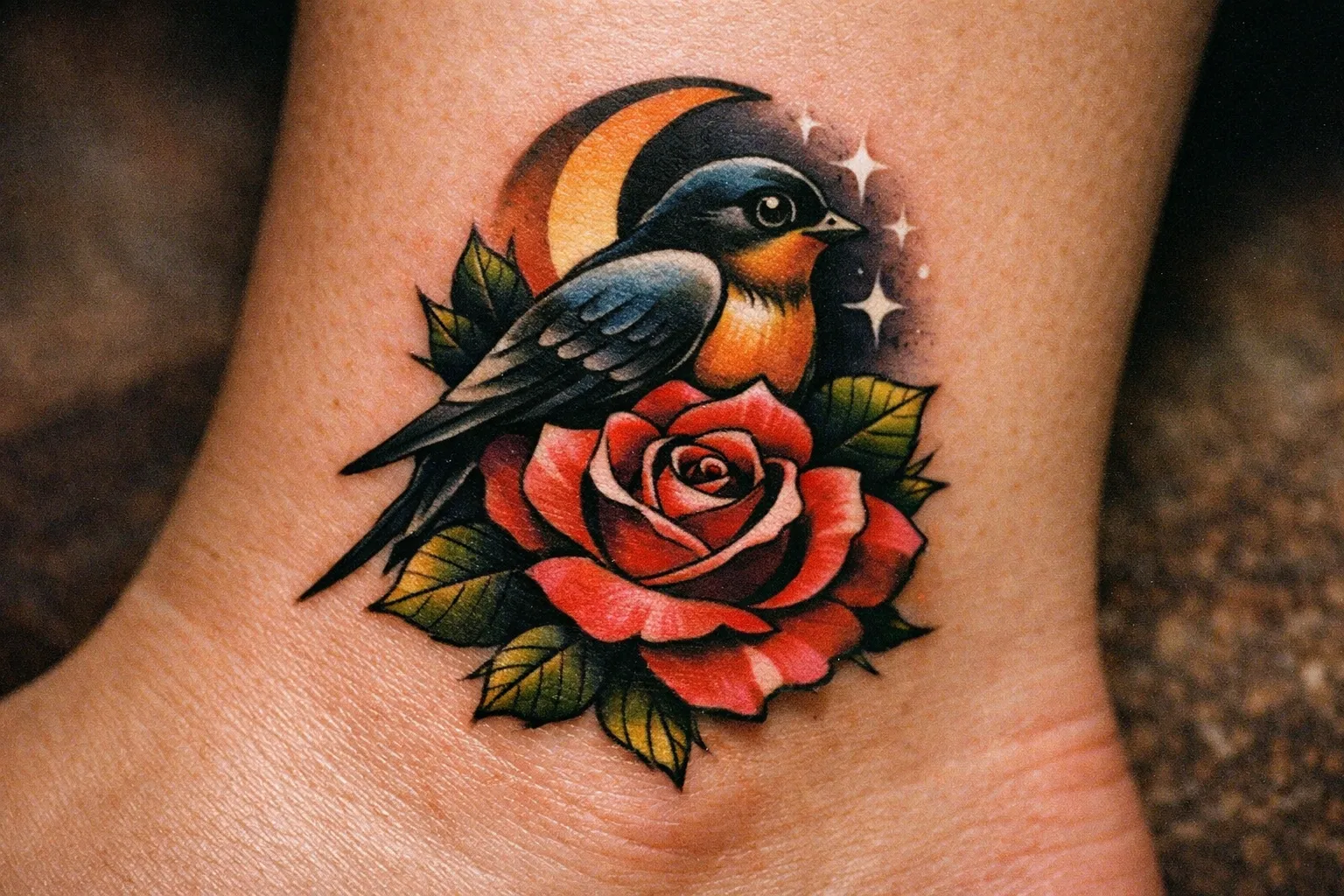 A neo traditional tattoo of a bird with a crescent moon and rose is shown on someone's ankle.
