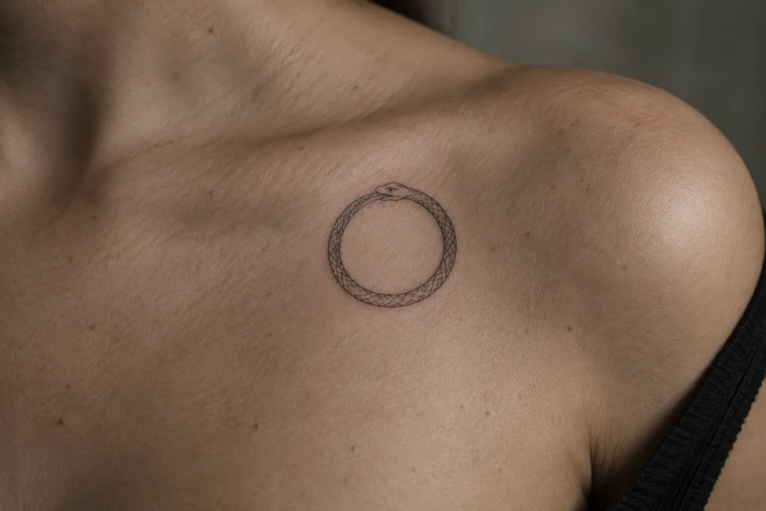 A person has a circular snake tattoo on their upper chest near the shoulder.
