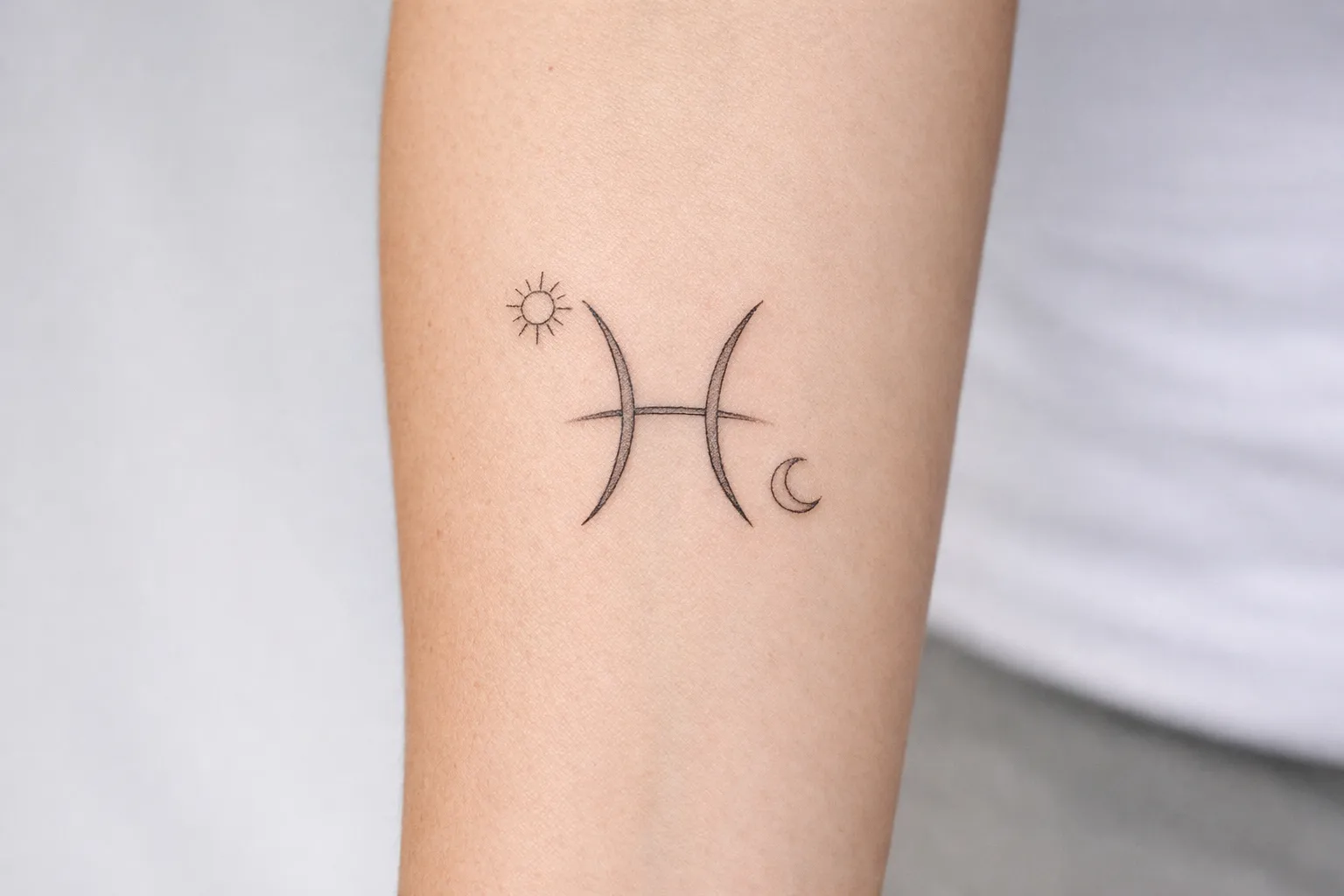 A Pisces zodiac symbol tattoo with a sun and moon design on a person's forearm.