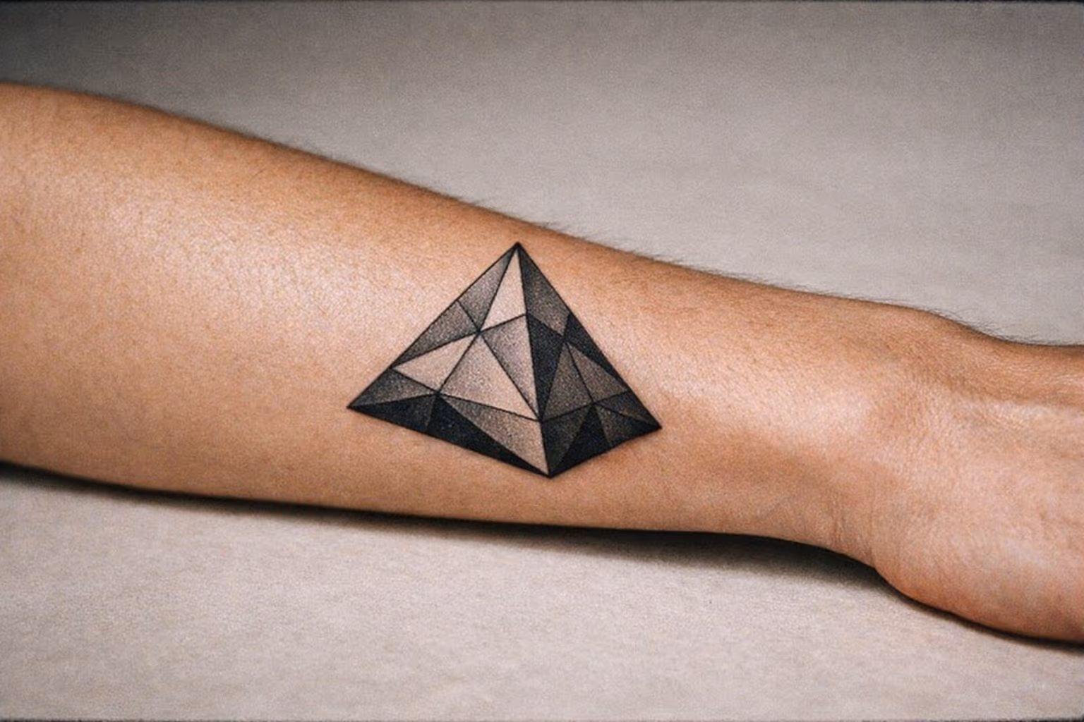 Editorial close-up of a forearm with a geometric pyramid tattoo in black ink