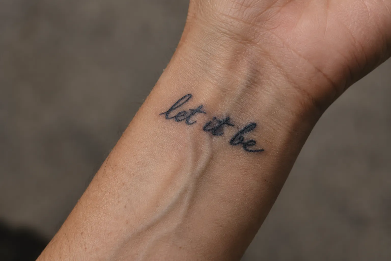 A cursive 'let it be' tattoo on the inside of a wrist.