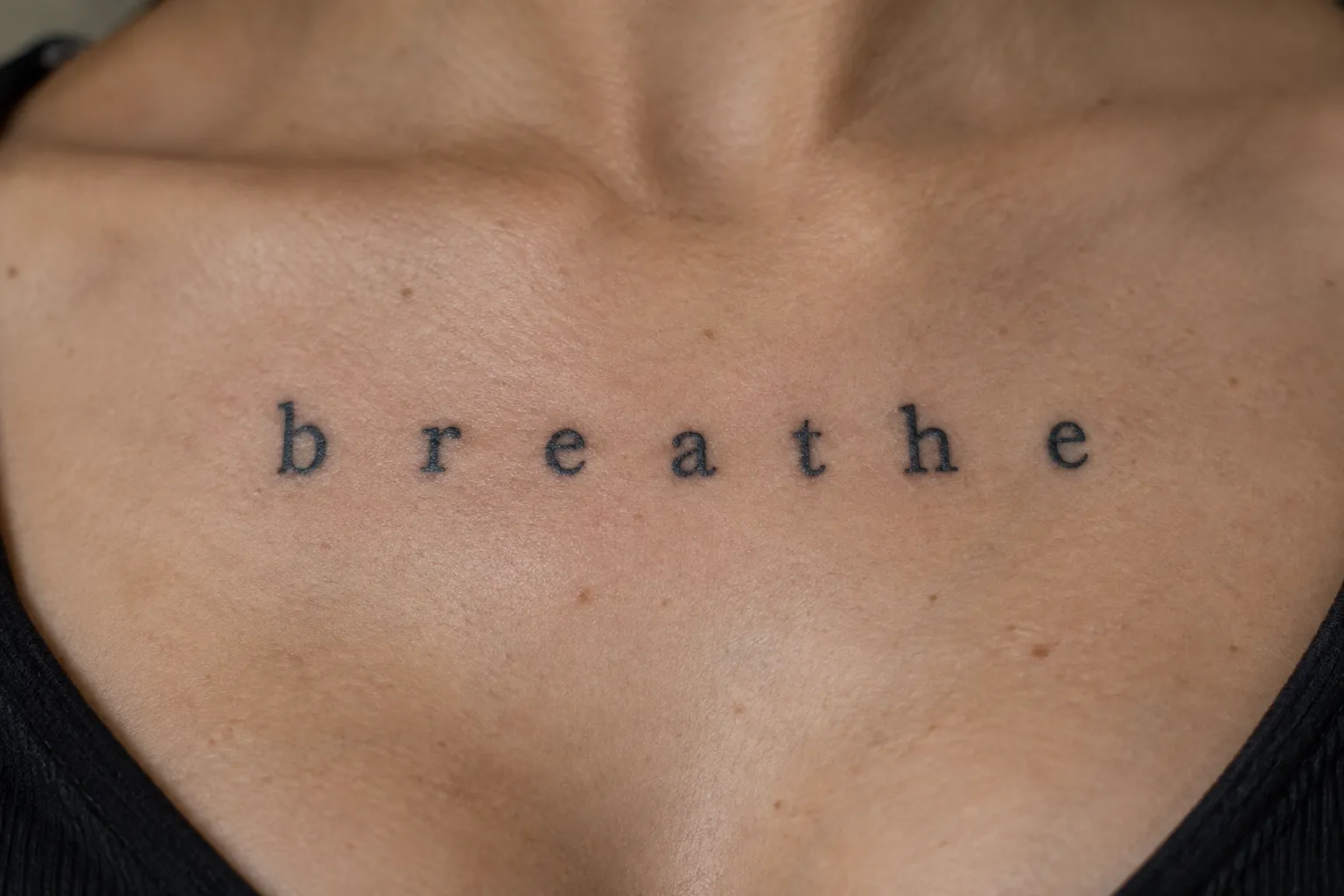 A person has the word 'breathe' tattooed across their upper chest.