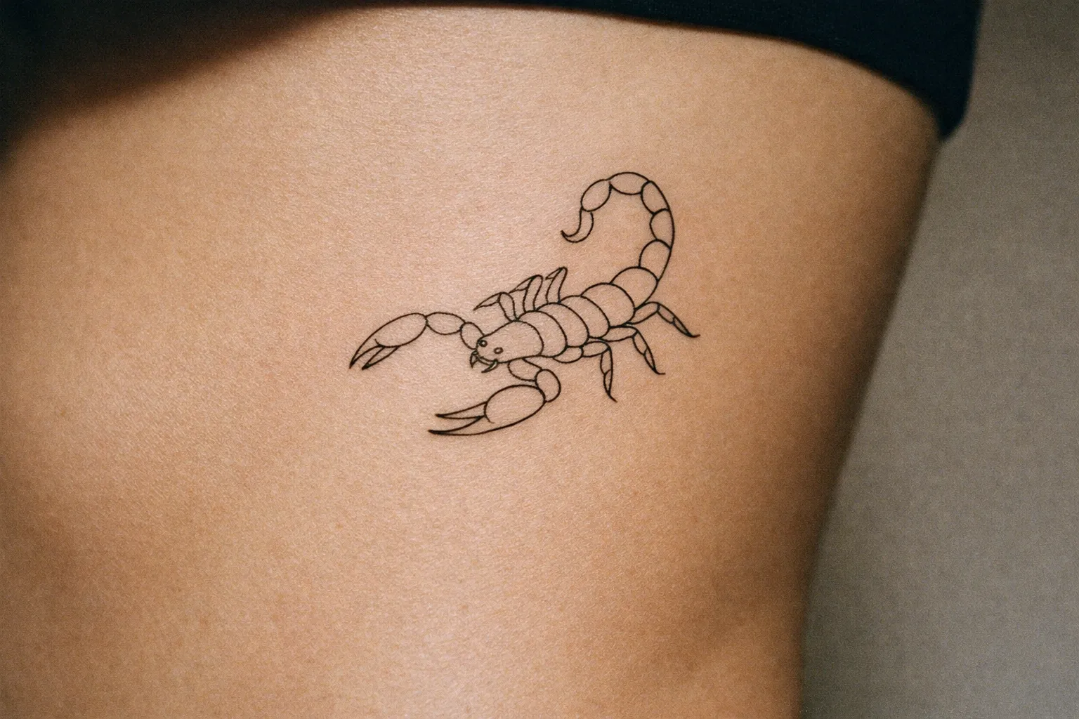 A fine-line outline scorpion tattoo on the side of a person's torso.