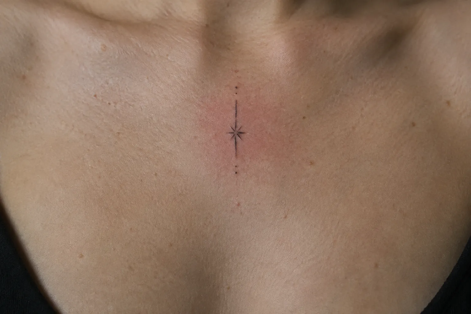 A small star stain tattoo at the center of the upper chest, the skin around it slightly pink.