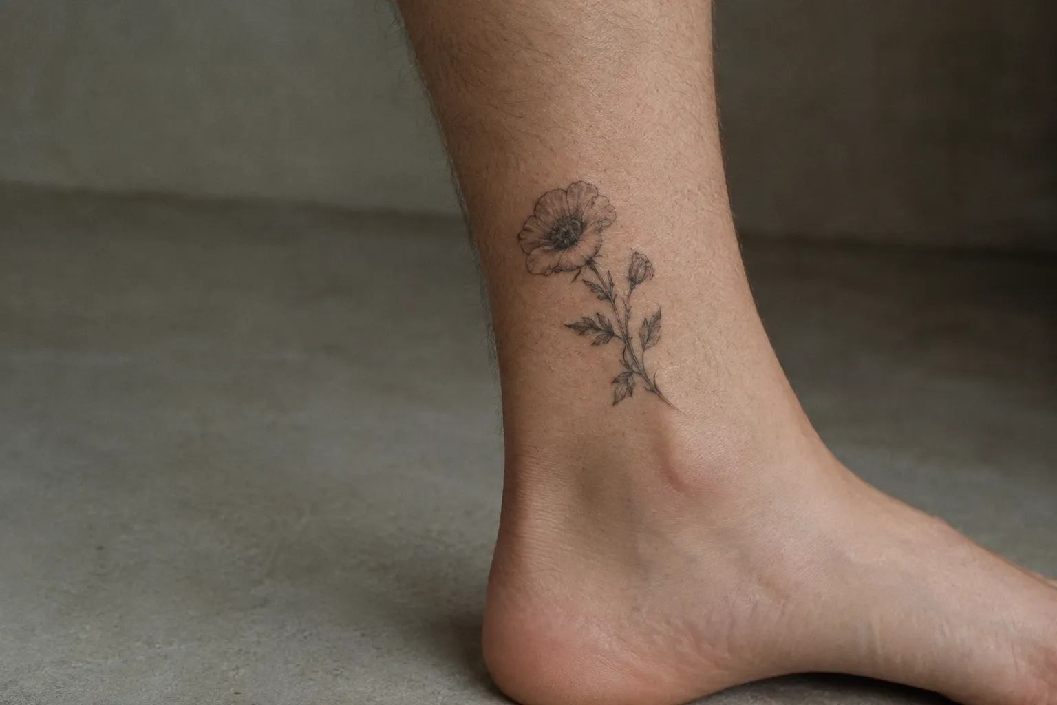 A small flower tattoo sits on the ankle above a bare foot.