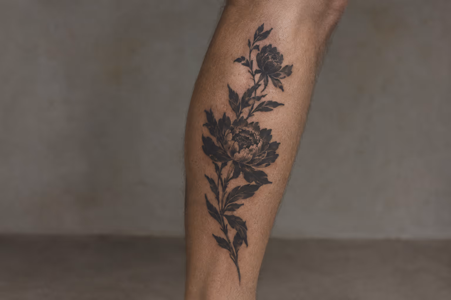 A floral tattoo runs along a person's lower leg against a plain wall.