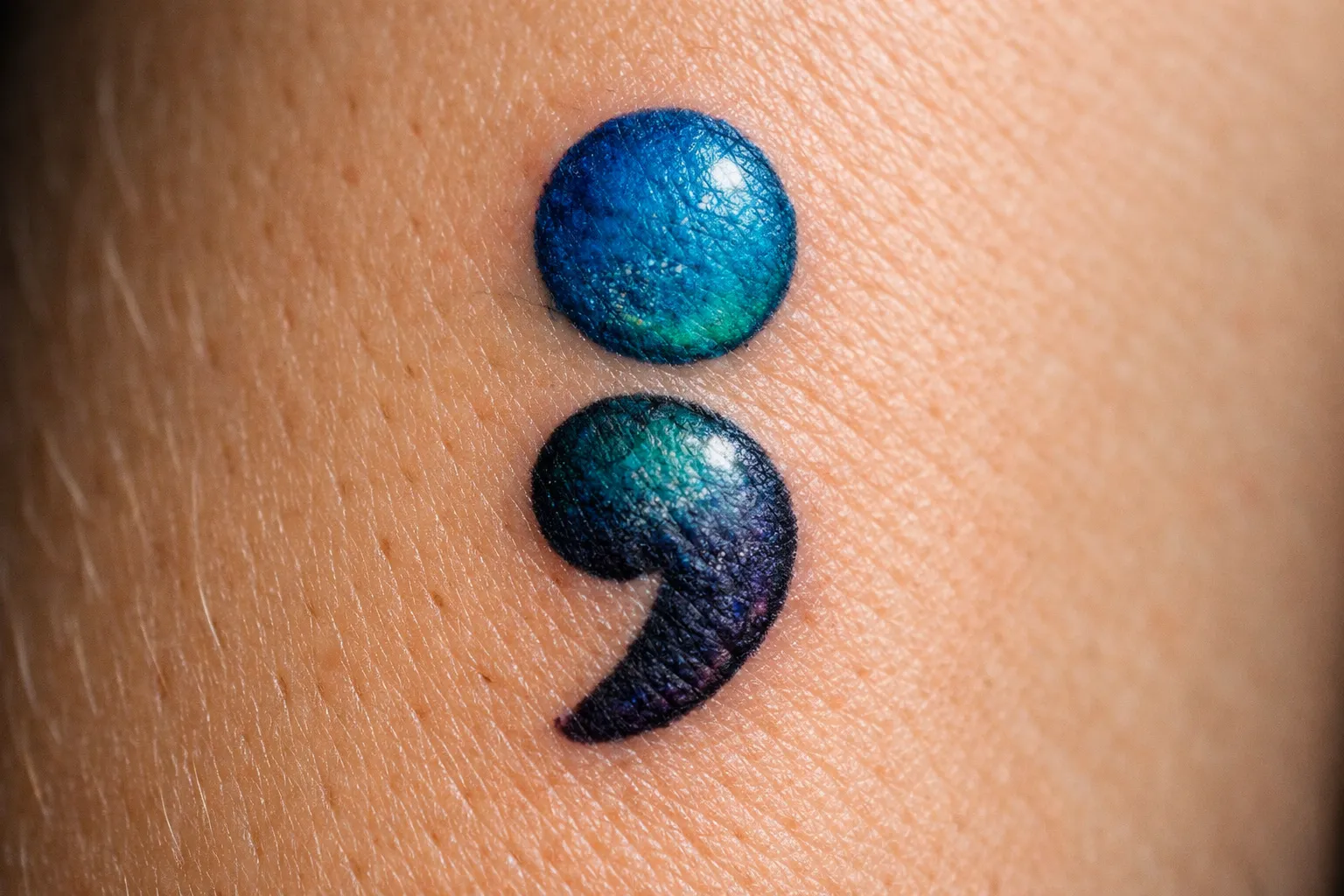 A blue and purple semicolon tattoo is shown on bare skin.