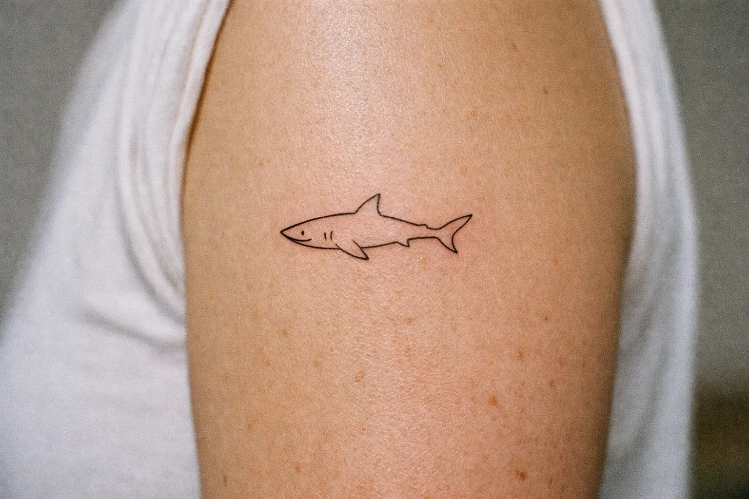 A simple shark outline tattoo on a person's upper arm.