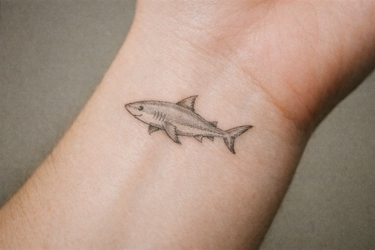 A small shark tattoo is inked on the inside of a person's wrist.