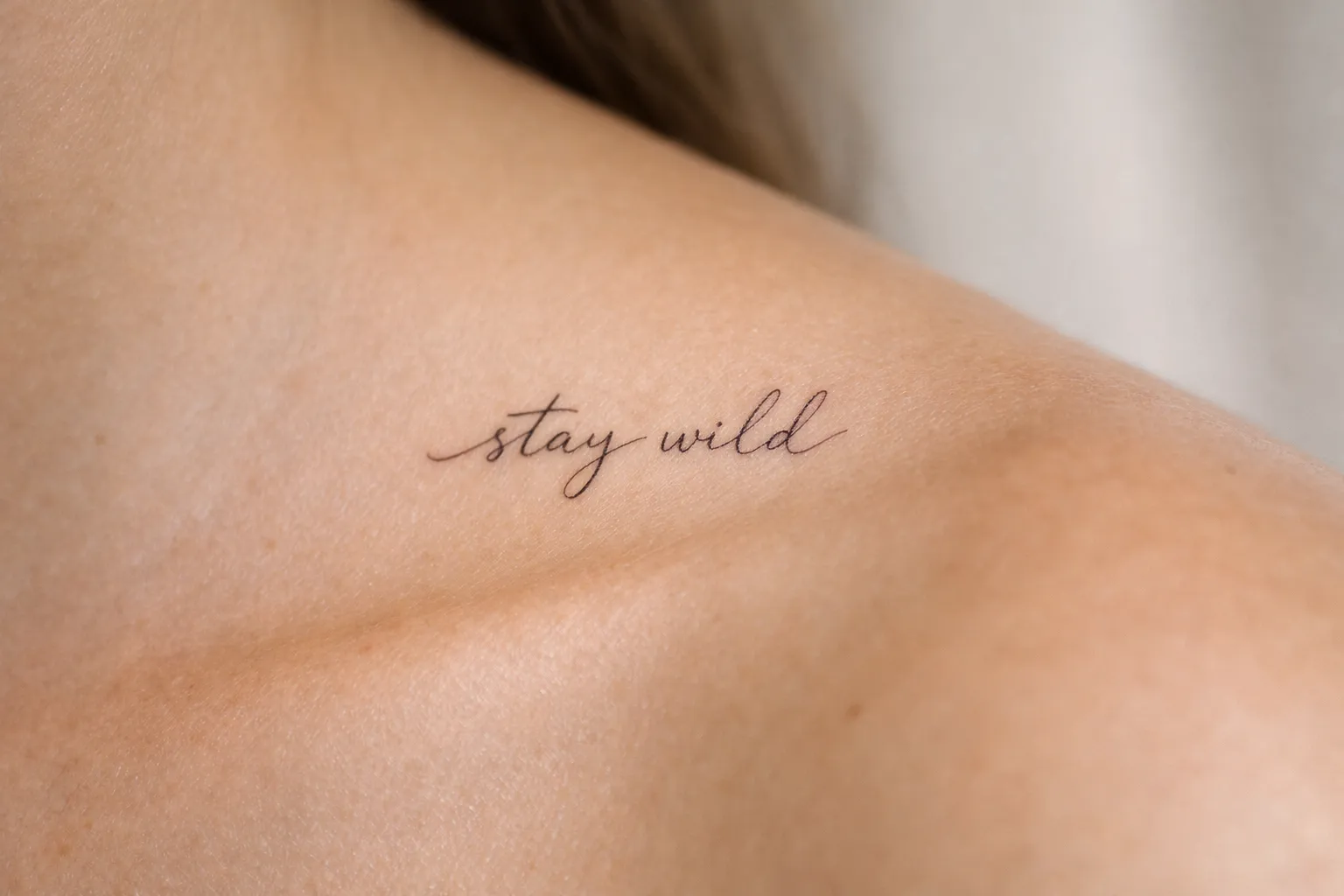 A delicate script tattoo reading 'stay wild' on a person's shoulder.