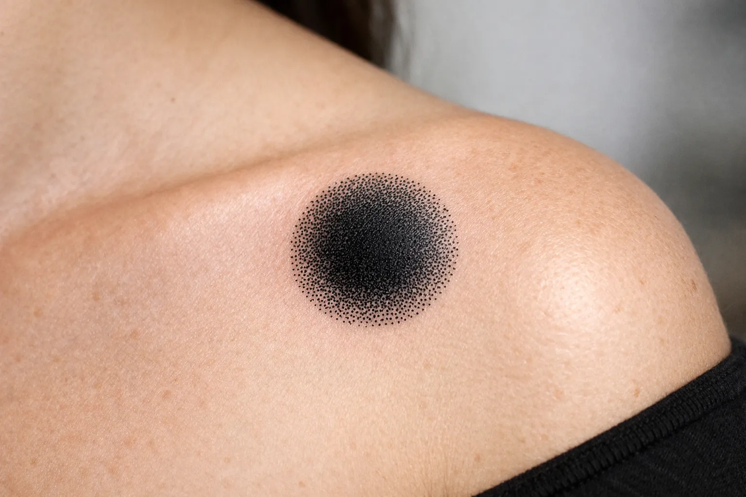 A black dotwork circle tattoo on a person's shoulder.