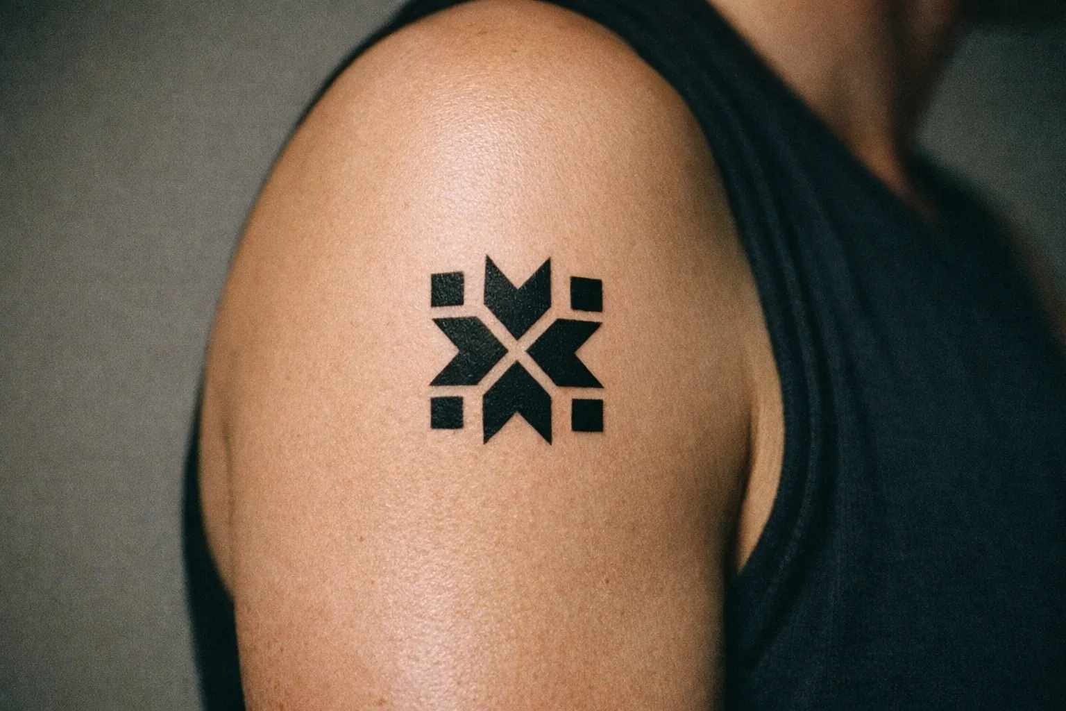 Geometric black tattoo on an upper arm in a sleeveless shirt.