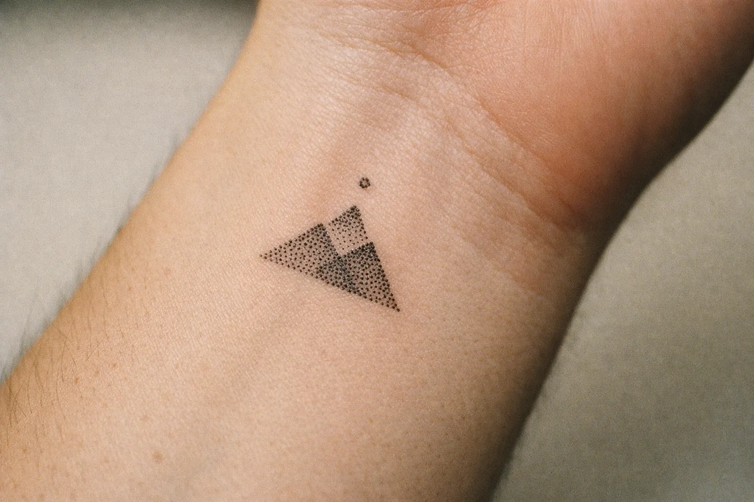A small geometric mountain tattoo is inked on the inside of a person's wrist.