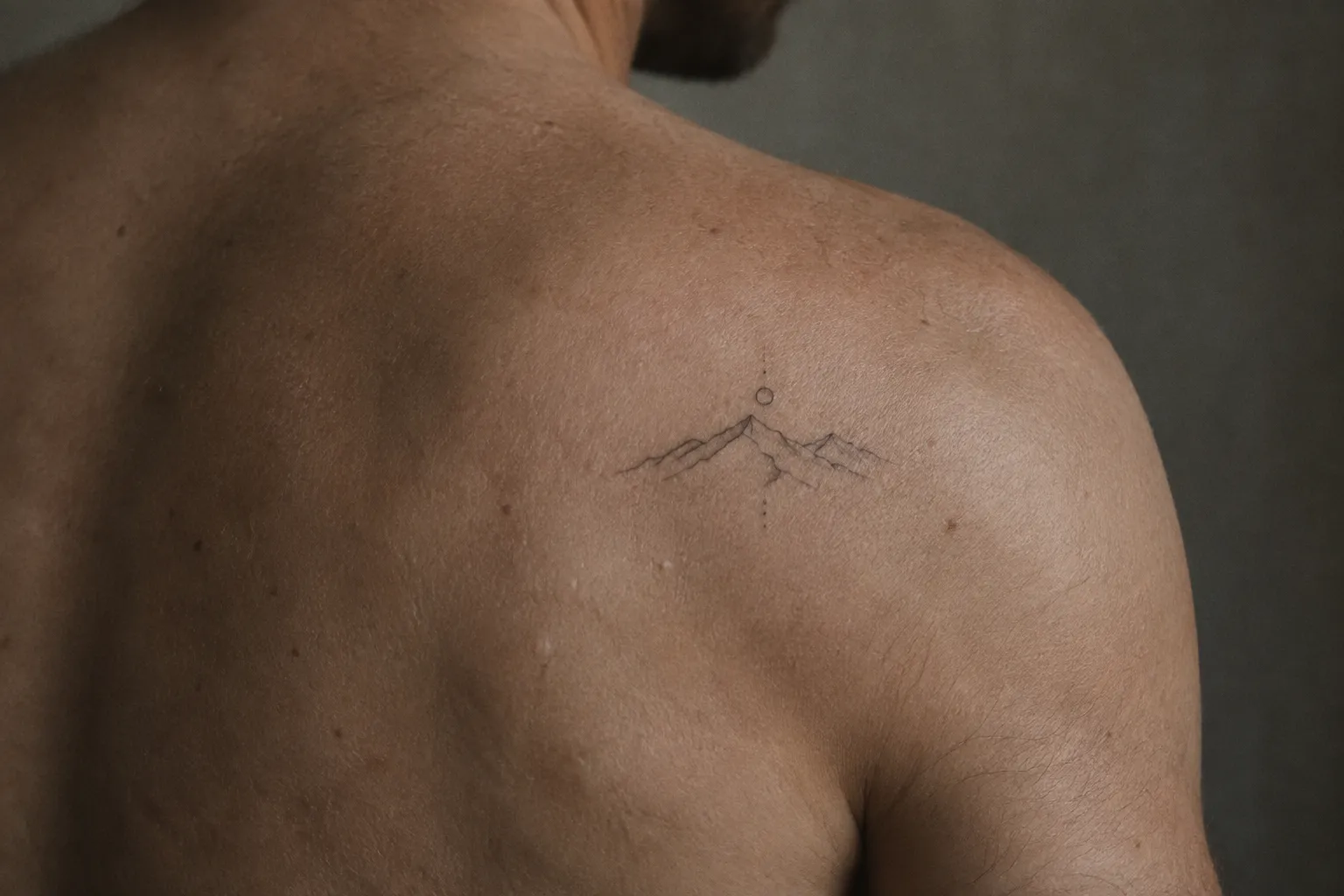 A man has a small mountain tattoo on his shoulder.
