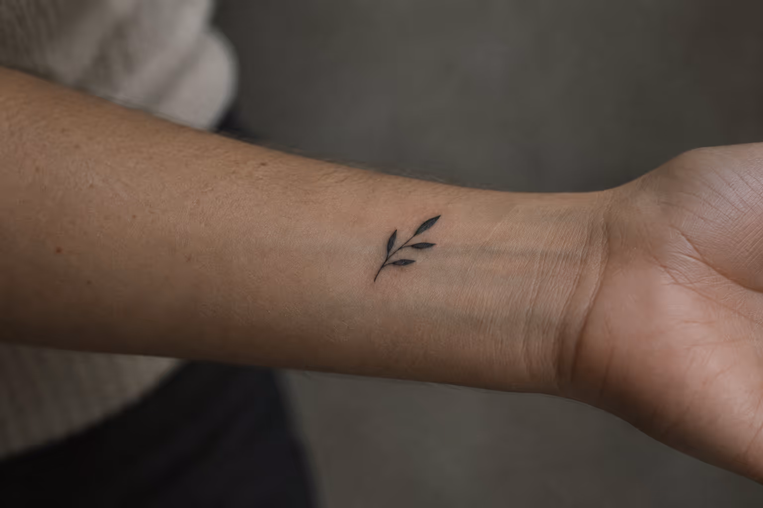 A small leafy branch tattoo sits on the inner wrist of an outstretched arm.