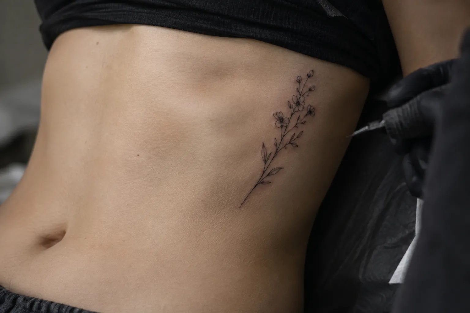 A person receives a delicate floral tattoo on their side abdomen in a tattoo studio.