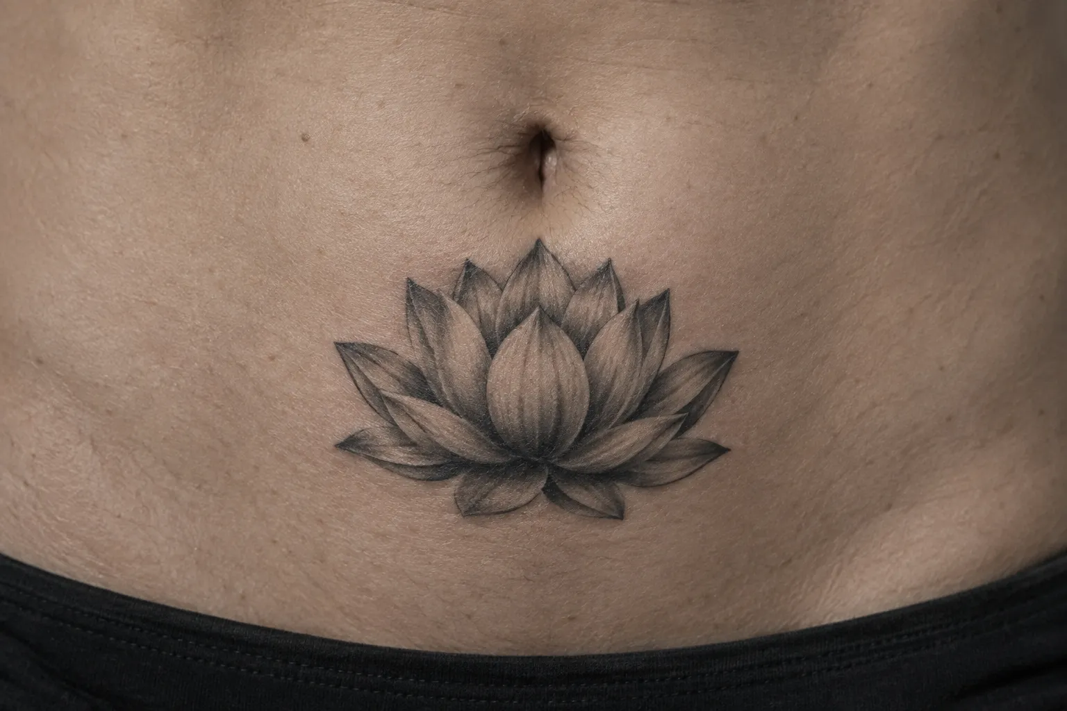 A lotus tattoo sits on a person's lower abdomen beneath the navel.