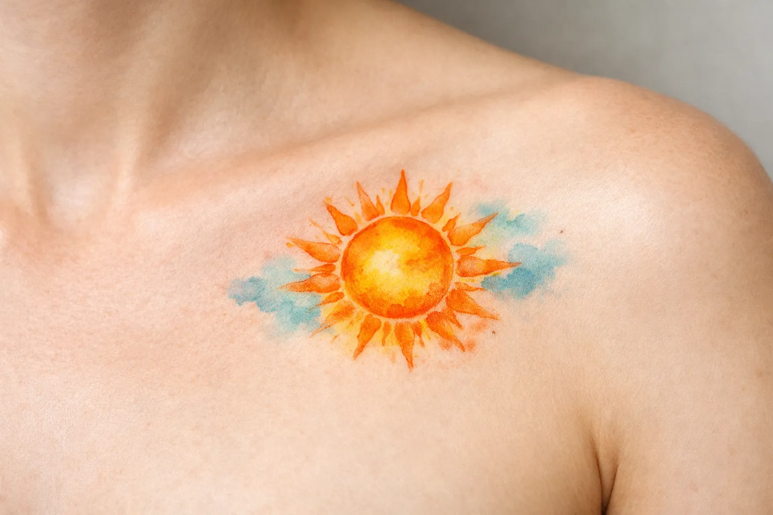 A vibrant sun tattoo with blue accents on a person's upper chest near the collarbone.