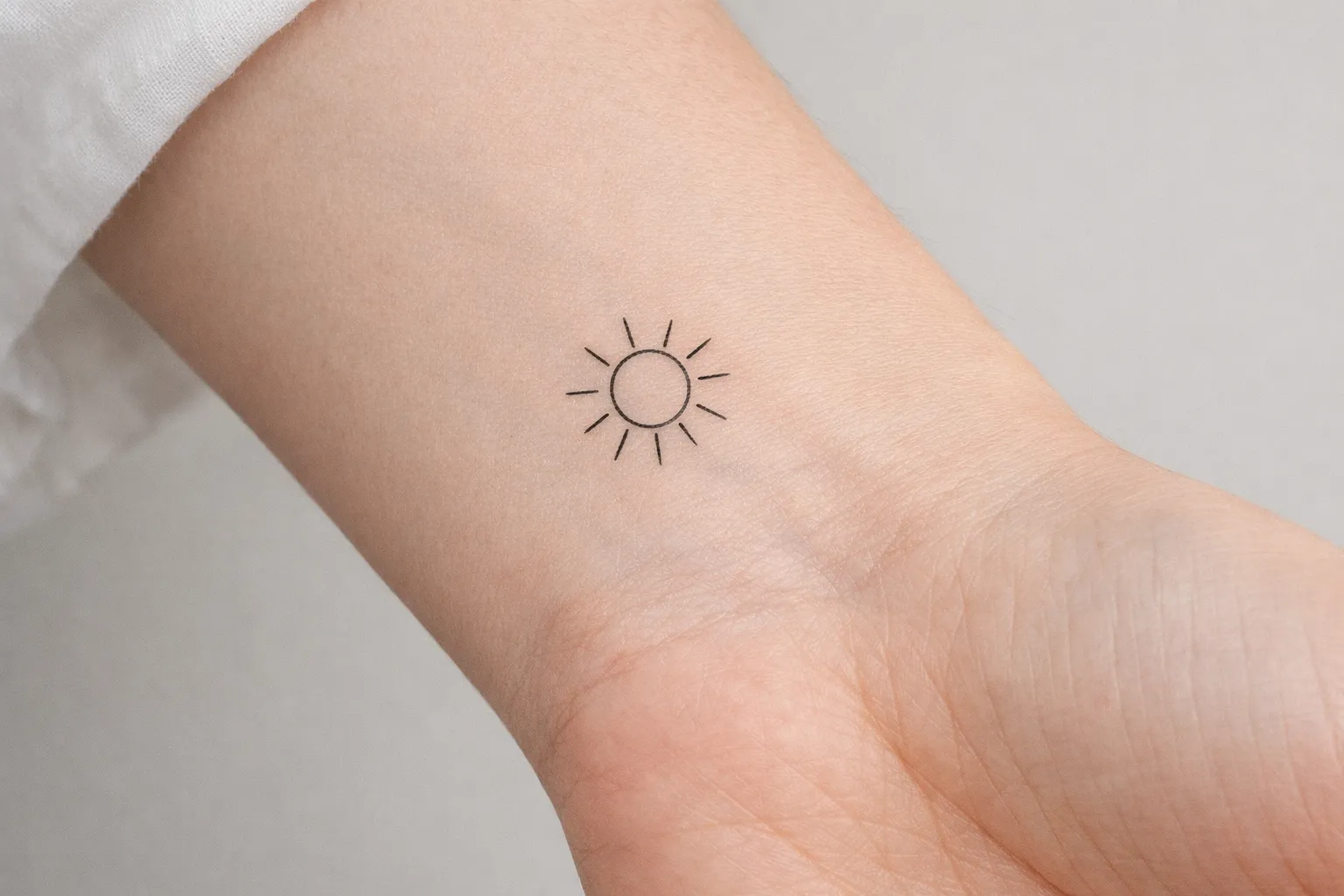 A simple sun tattoo is visible on the inner wrist of a person's arm.