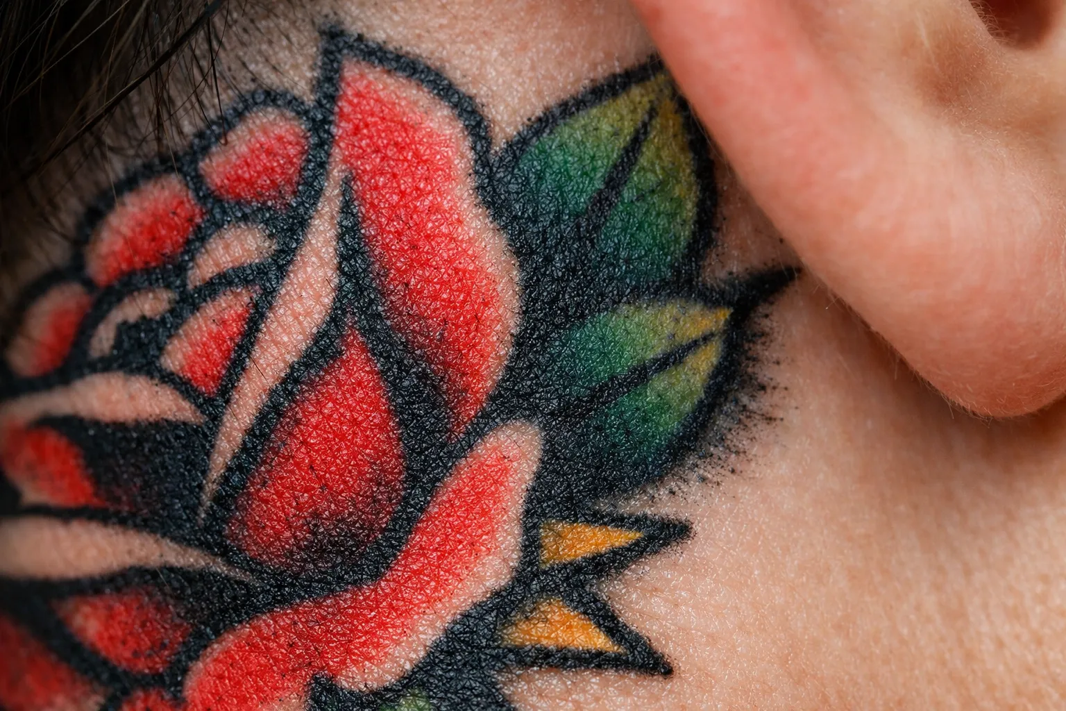 A colorful rose tattoo is inked on the skin near a person's ear.