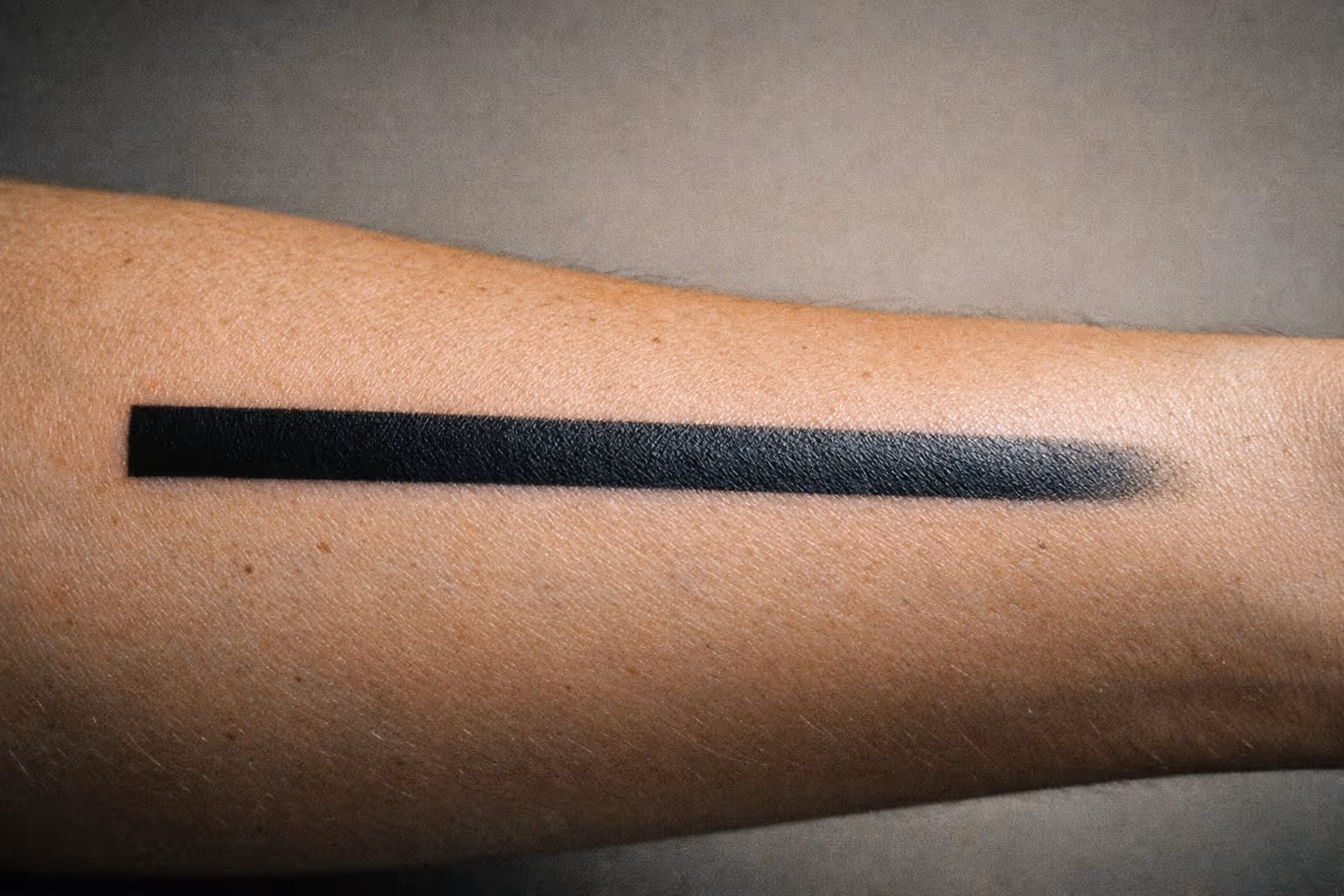Editorial close-up of a forearm tattoo showing a subtle blowout edge under soft studio lighting