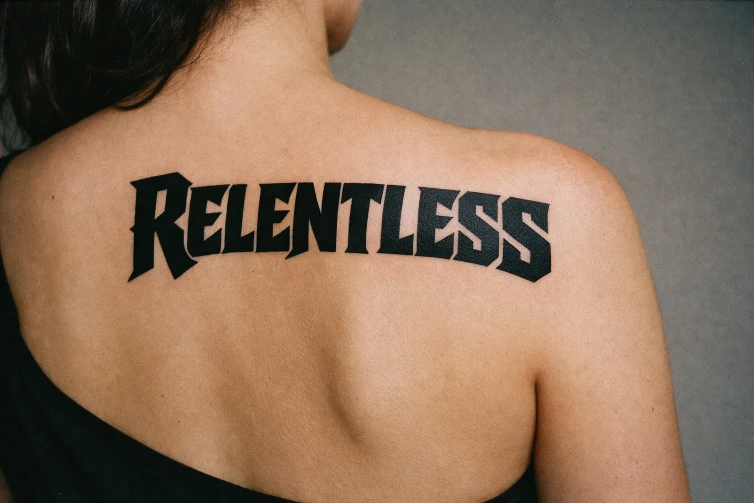 A person with a bold 'RELENTLESS' word tattoo across their upper back.