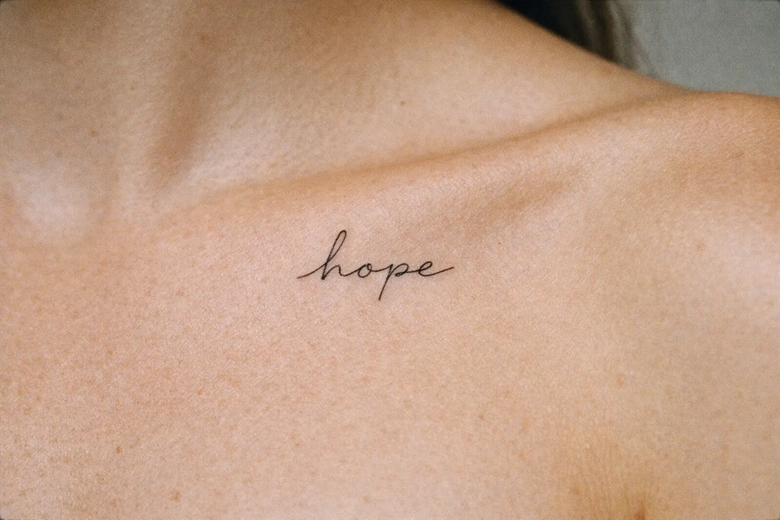 A cursive 'hope' tattoo inked on a person's collarbone.