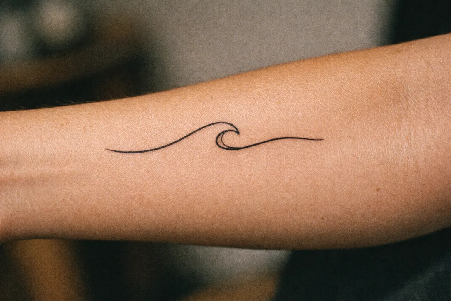Forearm displaying a minimalist single-line wave design
