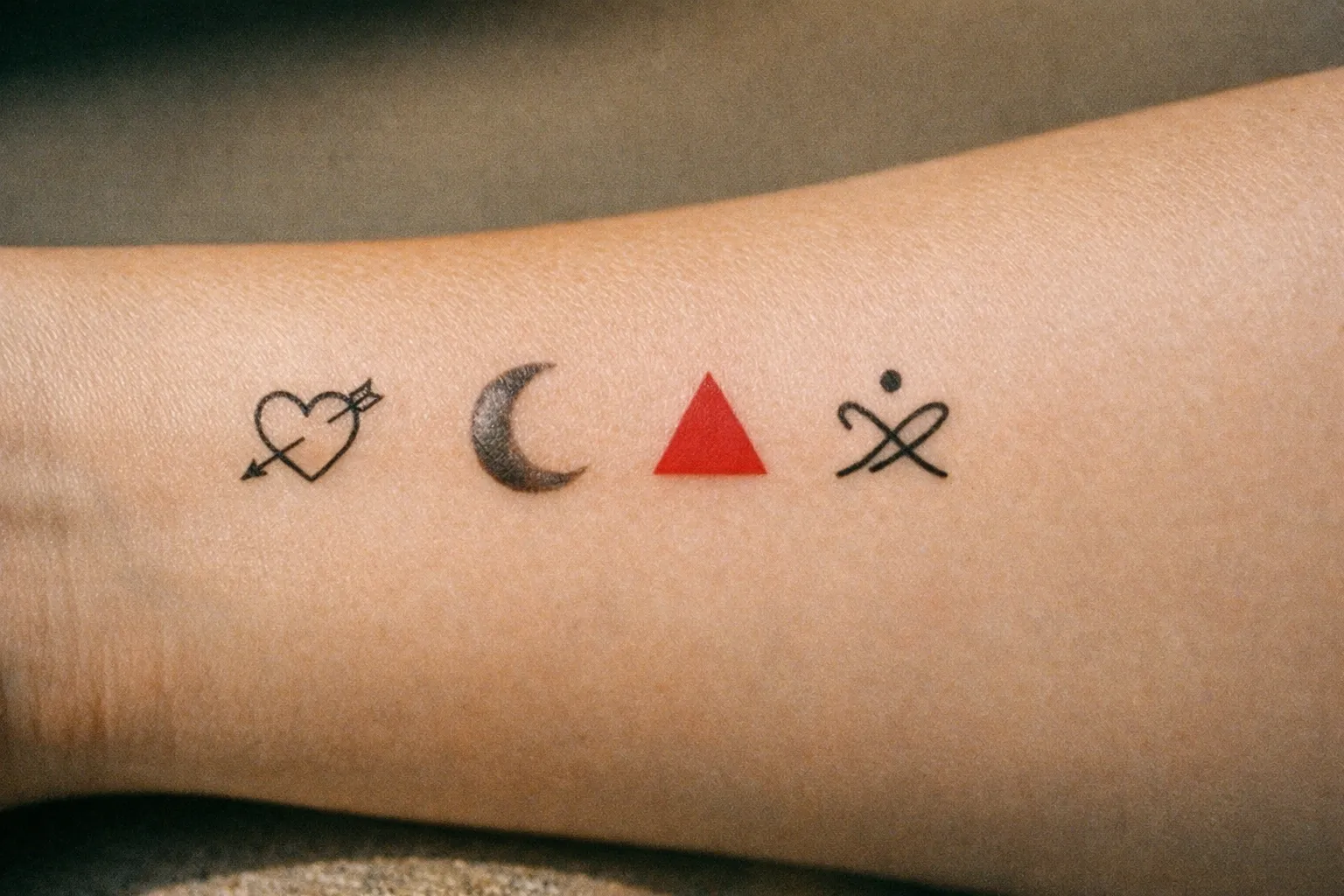 Forearm showing four small tattoos illustrating lining, shading, coloring, and an abstract symbol