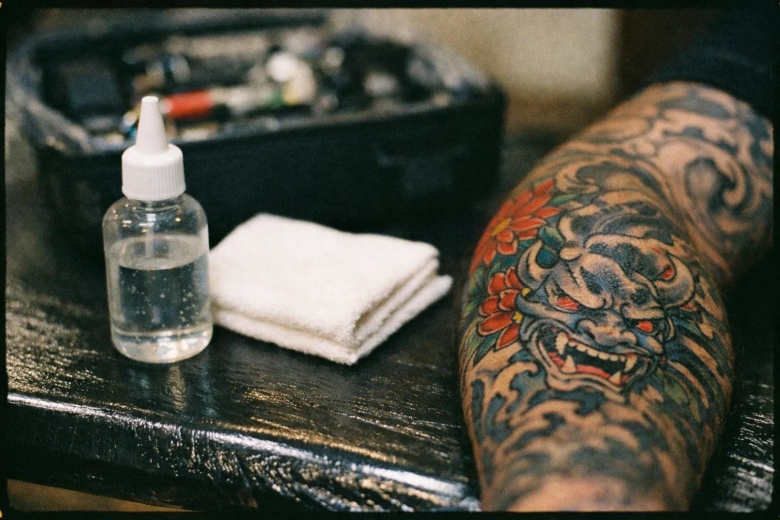 Forearm tattoo with maintenance items nearby: small bottle of lubricant and clean cloth, presented on a tidy studio surface