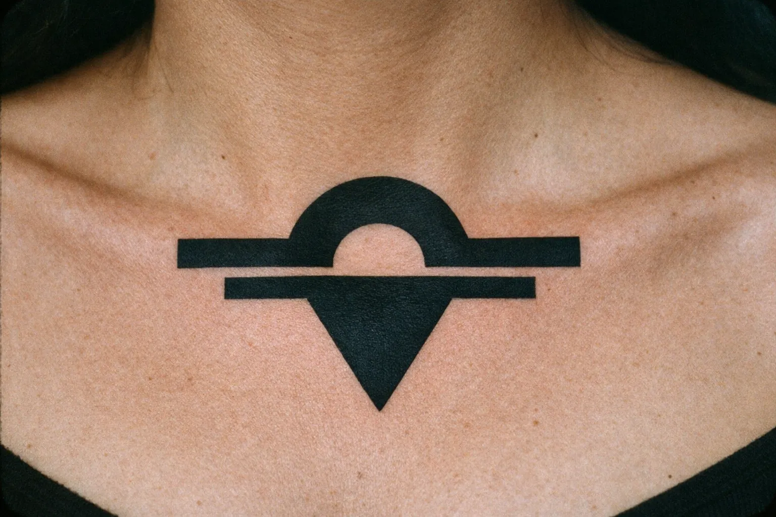 A person with a bold geometric black tattoo on their upper chest below the collarbone.
