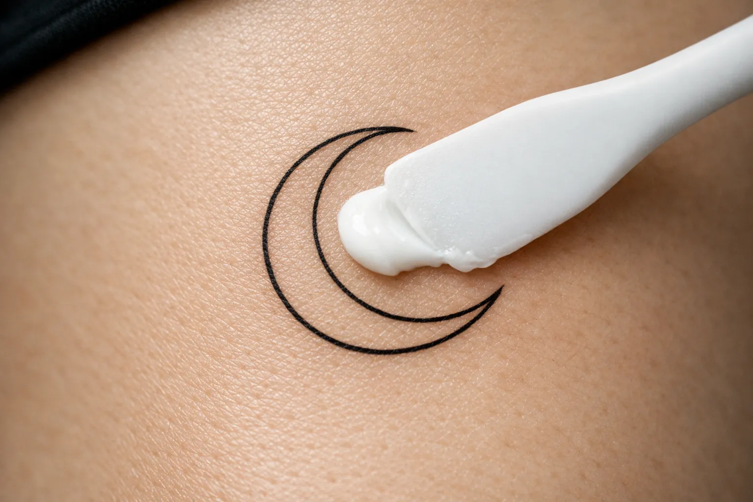 Tattoo lotion being applied to a crescent moon tattoo on bare skin.