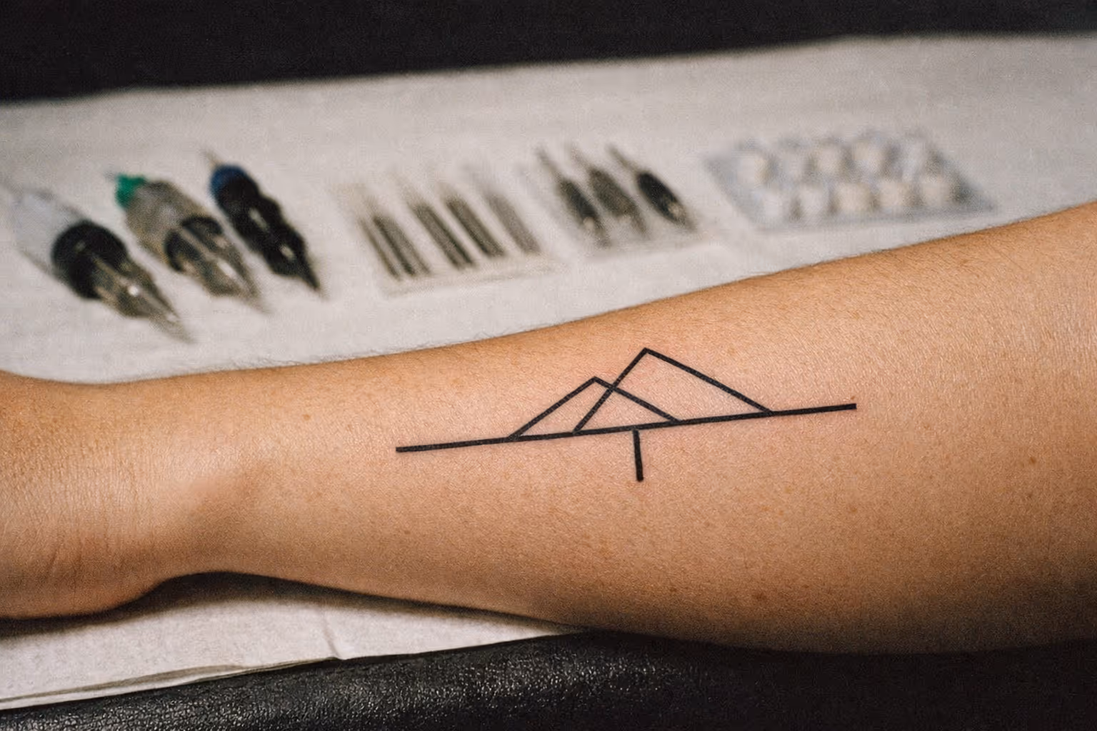 Editorial cover shot of a healed forearm tattoo with a display of needle configurations in soft focus