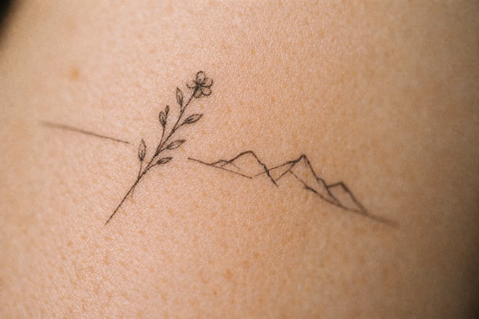 A delicate tattoo of a flower and mountains is shown on bare skin.