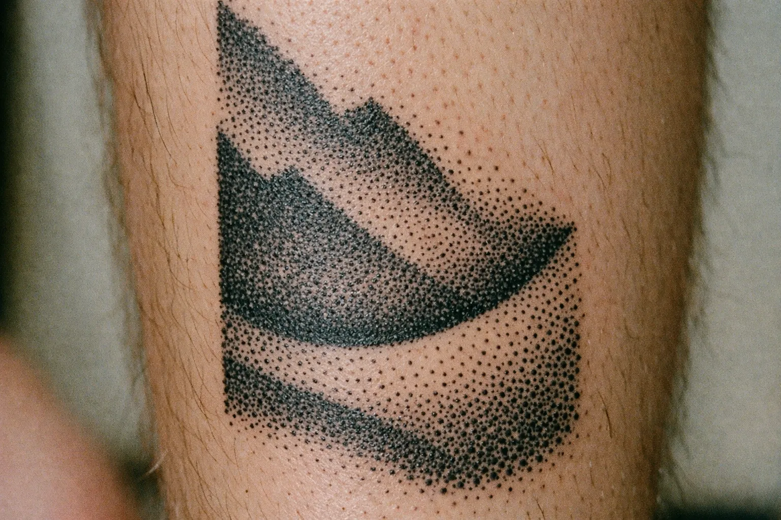 A geometric mountain tattoo in black dotwork style on a person's lower leg.