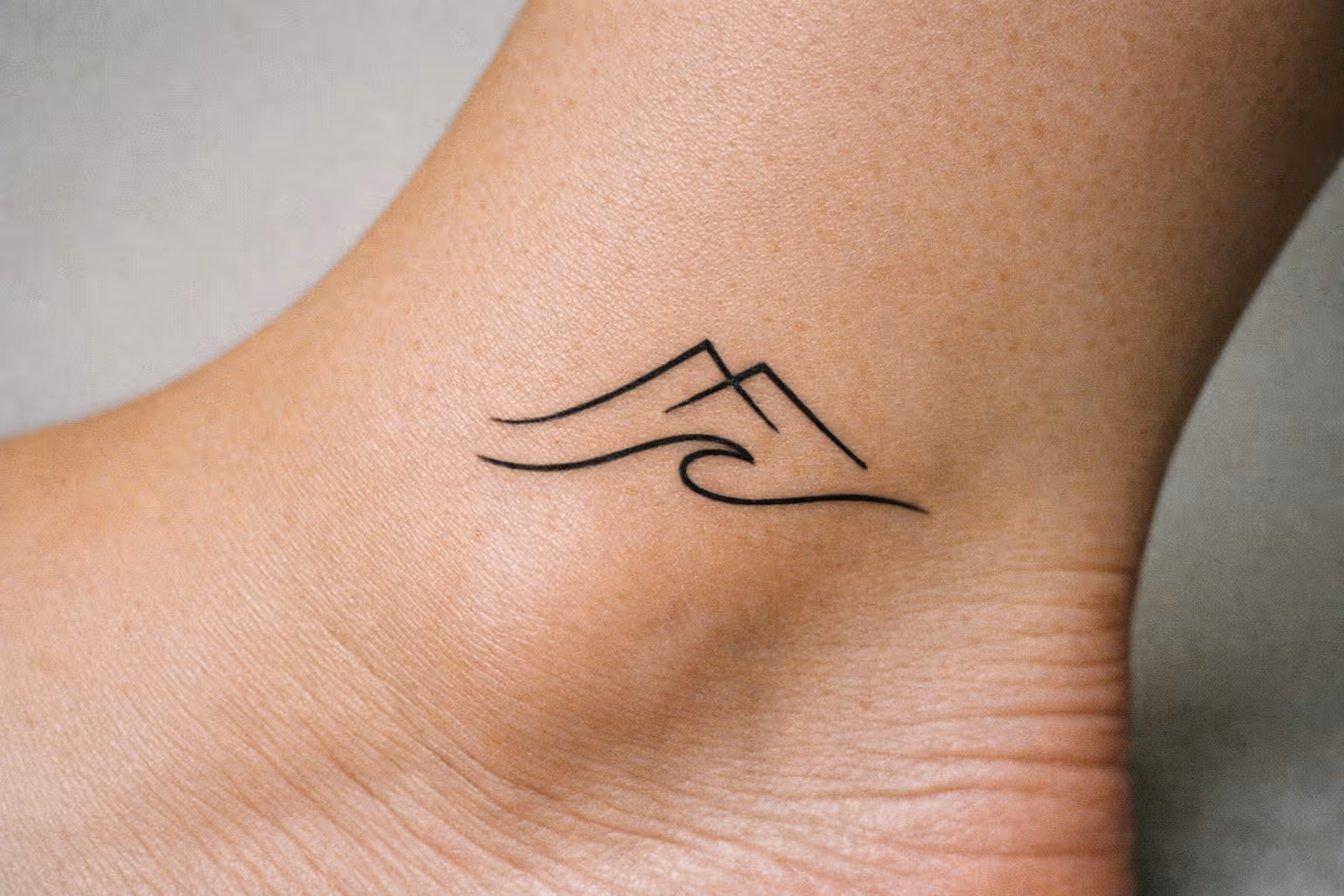 Minimalist mountain and wave tattoo on the side of an ankle.