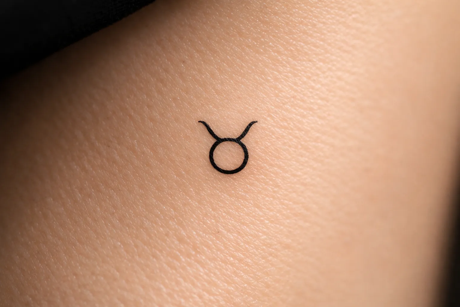 A small Taurus zodiac symbol tattoo is inked on a person's skin.