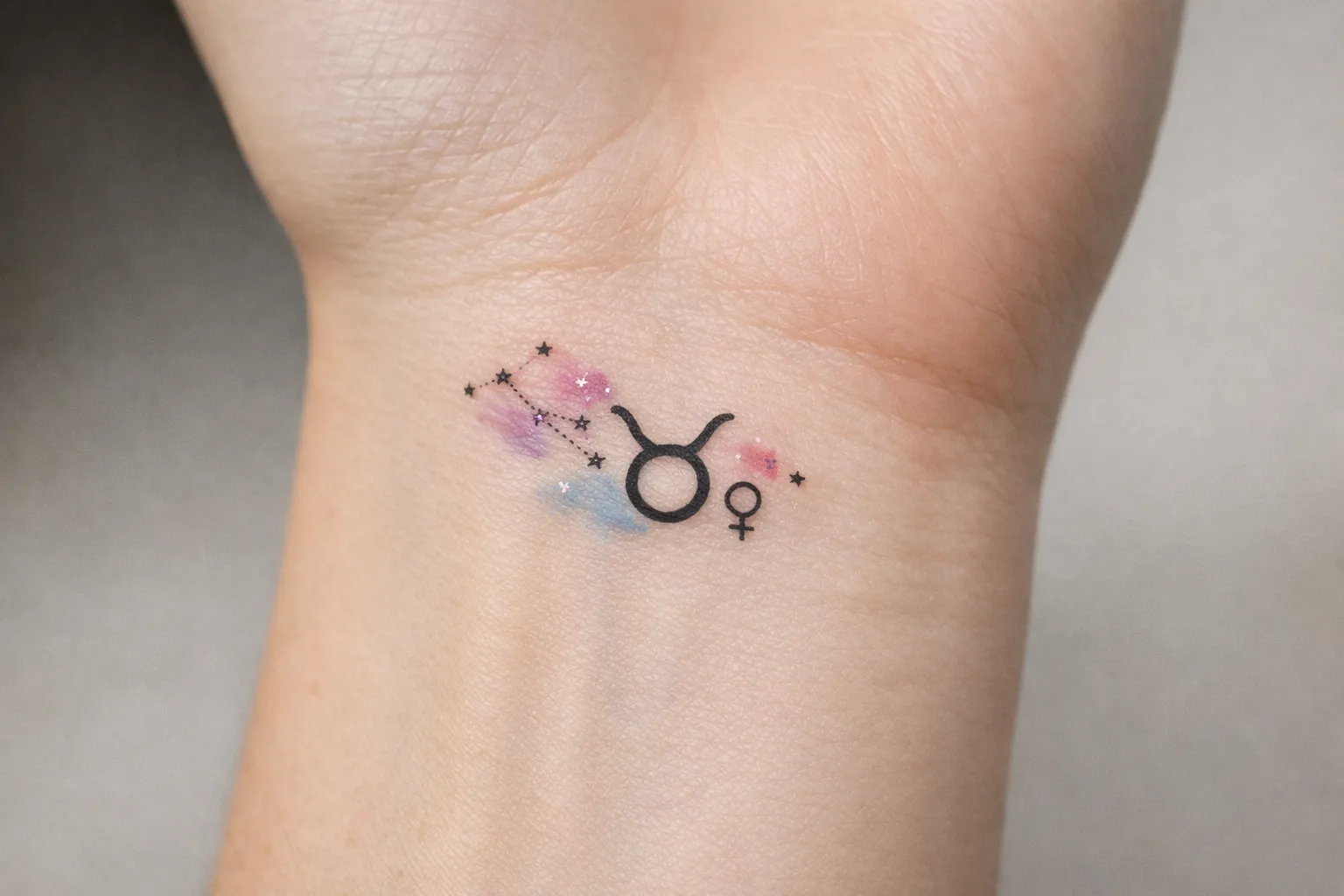 A small Taurus zodiac tattoo with constellation and colorful accents on a person's wrist.