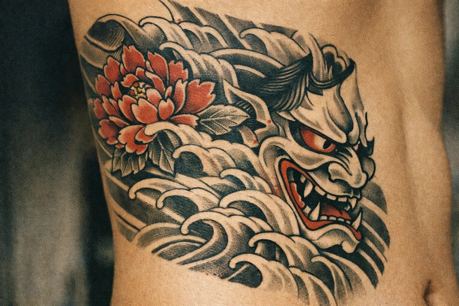 A traditional Japanese tattoo of a hannya mask and peony flower on a person's side torso.